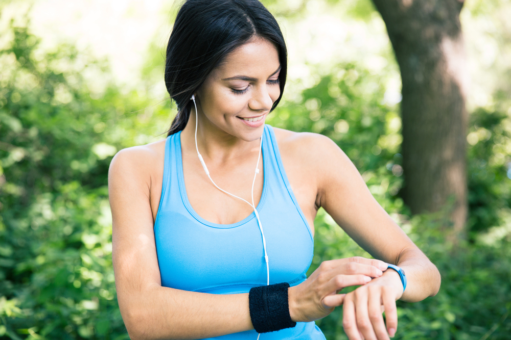 Smiling sporty woman in headphones using smart watch outdoors in park